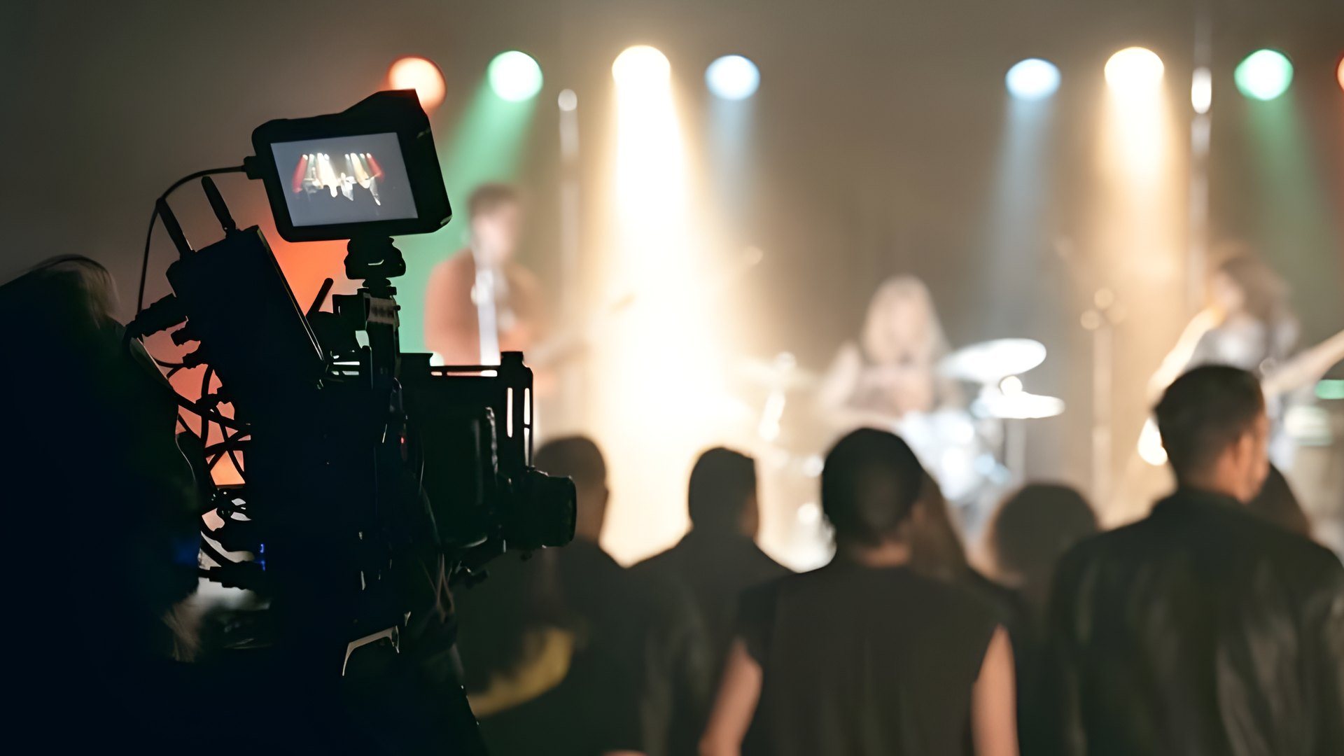Filmkamera i forgrunnen filmer et band på scenen med publikum foran, under opptak av Heroinbyen